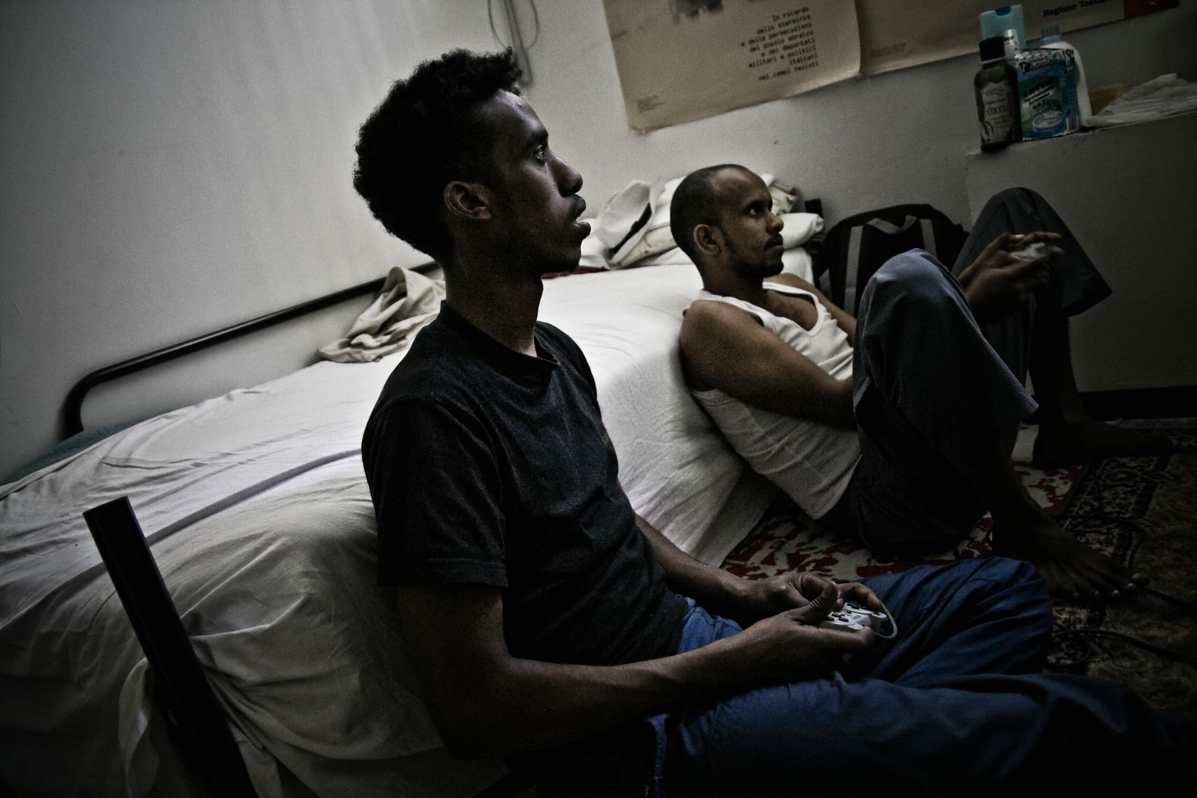 ITALY. Florence, 20th June 2011. Two Somali refugees playing with an electronic game console inside a former office building occupied by Somali and Eritrean refugees.