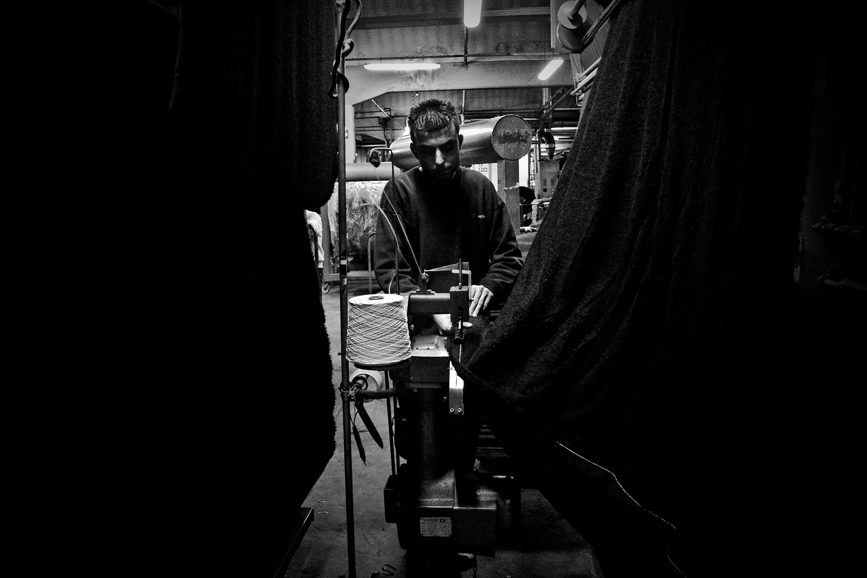 ITALY. Montemurlo (Prato), 31st March 2009. A worker hems a tissue coming out from a finising machine.